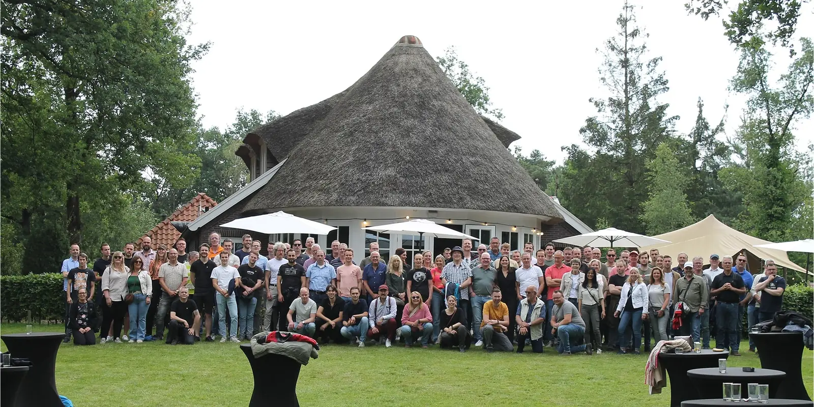 Groepsfoto van de medewerkers van De Spiraal en Tribelt op het grasveld bij een boerderij met rieten dak