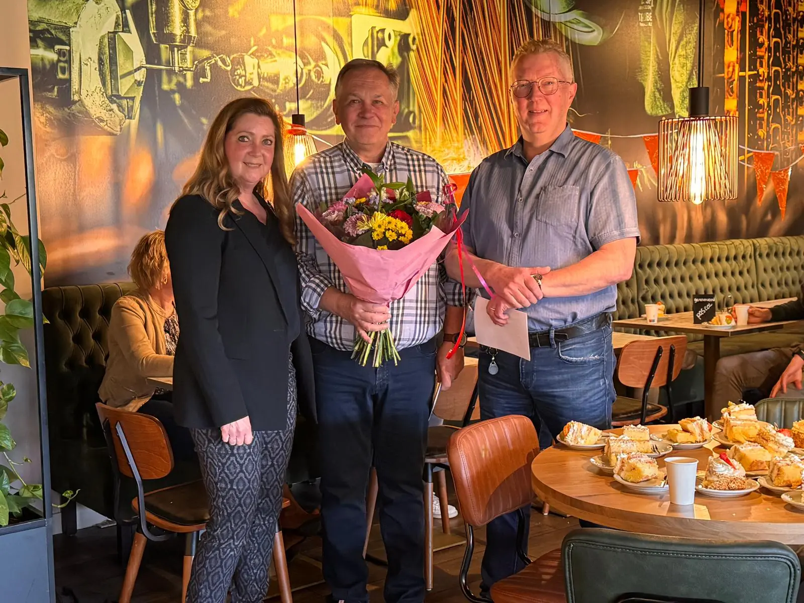 Pascal met een bos bloemen tussen twee collega's in een restaurant