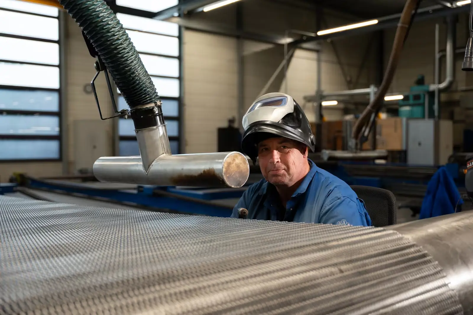 Productiemedewerker met lashelm achter een rol metalen band